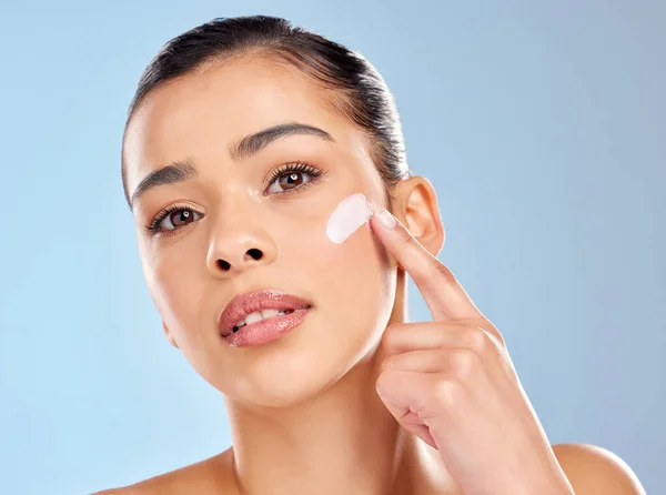 stock image Dont hate, exfoliate. Studio portrait of an attractive young woman applying moisturiser on her face against a blue background