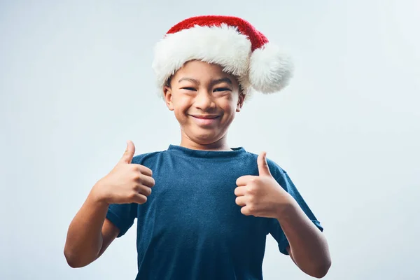 크리스마스 트리에서 스튜디오는 모자를 배경에 엄지손가락을 보이는 귀엽고 소년의 사진을 — 스톡 사진
