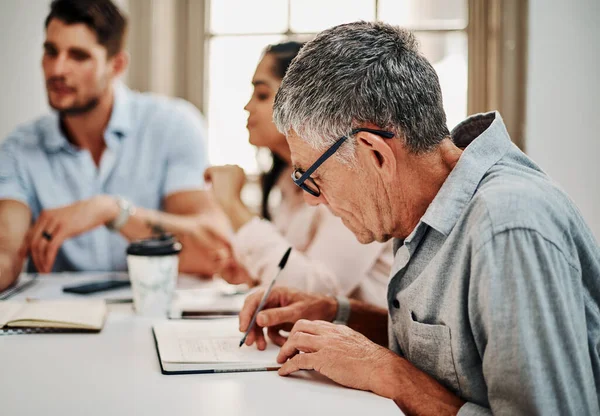 stock image Record everything, you might need it later. a mature businessman writing notes during a meeting with colleagues in a modern office