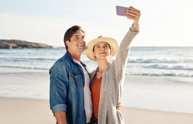 Plaj selfieleri en iyisidir. Sahilde selfie çeken orta yaşlı bir çift.