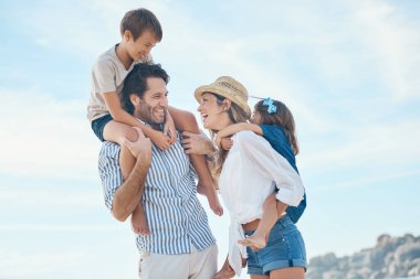 Bir ailenin sevgisi, hayattaki en büyük lütuftur. Mutlu genç bir çift kumsalda keyifli bir günde iki çocuğunu taşıyor.