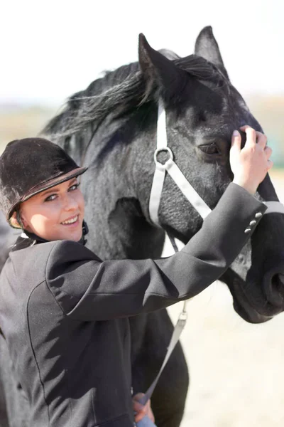 乗馬の訓練や競争の場で馬のライダー トレーナーの肖像画や女性 女性の競争相手とヘルメットに乗る前に動物を撫でる女の子の笑顔で馬を安定表示します — ストック写真