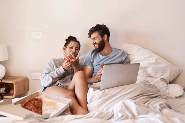 映画マラソンとピザ もっとロマンチックになるの ノートパソコンを使ってピザを食べながら家のベッドでリラックスしている幸せな若いカップルは — ストック写真