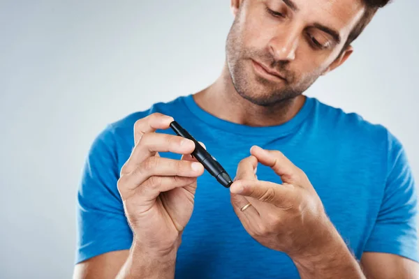 stock image Quick and easy. Studio shot of a carefree young man taking a blood sample from a syringe out of his finger while standing against a grey background