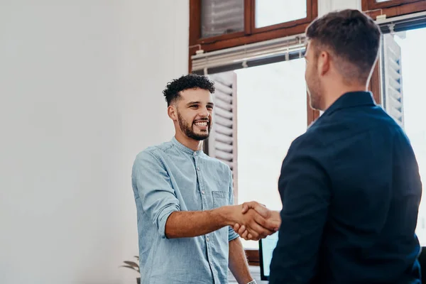 Welcome aboard an awesome business. two young businessmen shaking hands in a modern office