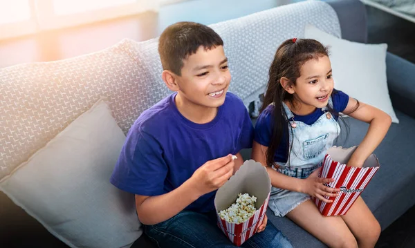 画面にロックされたままにするエンターテイメント 家で映画を見ながらソファに座ってポップコーンを食べる2人の若い子供の高い角度ショット — ストック写真