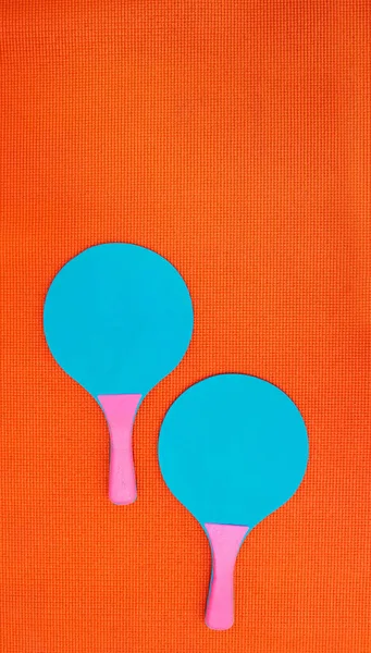谁想玩 两个乒乓球蝙蝠放在工作室的橙色背景上的高角镜头 — 图库照片