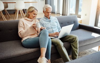 Emeklilik için daha iyi bir yol olabilir mi? Yetişkin bir çift evdeki kanepede dizüstü bilgisayar kullanıyor.
