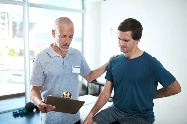 stock image Tell me more about the pain youre feeling. a handsome mature male physiotherapist having a consultation with a patient