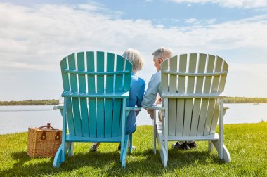Emeklilik hedeflerine ulaşılabileceğinin kanıtı. Sevecen bir son sınıf çifti dışarıda birlikte sandalyede dinleniyor.