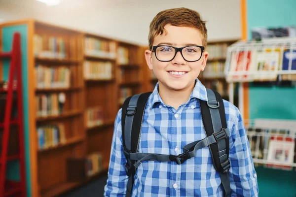 今日は新しい学校での最初の日です 昼は図書館の中に立ち 通学用のかばんを持った陽気な少年の肖像画 — ストック写真