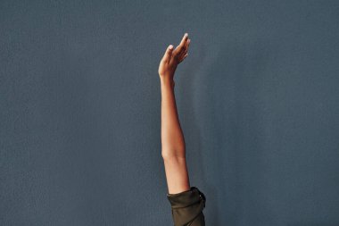 Zirveye ulaş. Tanımlanamayan bir kadının gri bir arka plana el kaldırırken çekilmiş bir fotoğrafı.
