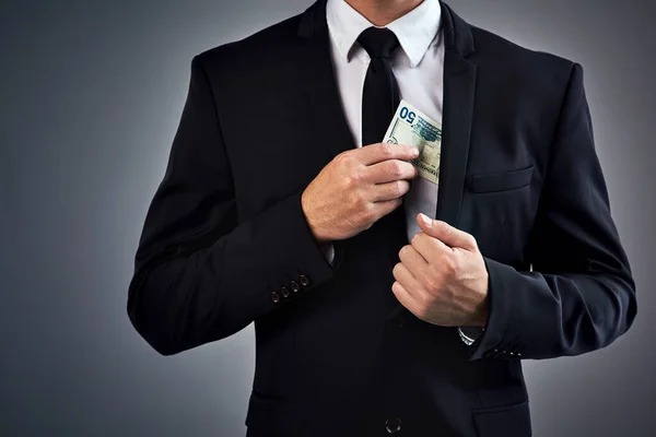 以诚信为代价获利 拍下了一个商人在灰色背景下把钱藏在夹克里的剪影 — 图库照片