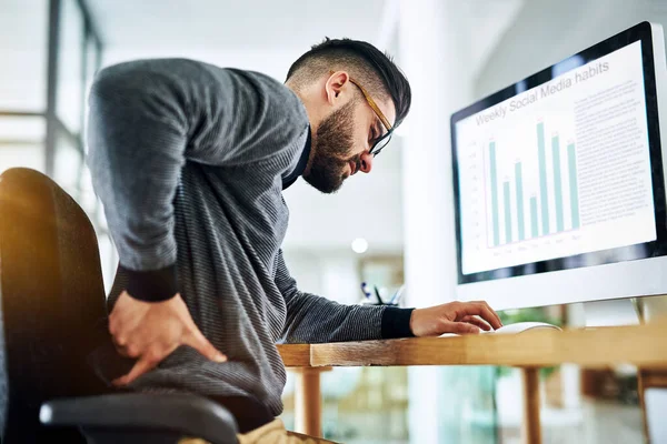 Sitting for too long can trigger unbearable back pain. a young designer suffering from back pain while working at his office desk