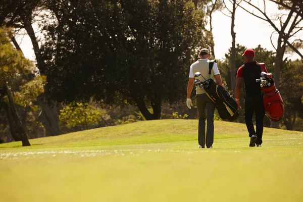 期待着下一场比赛 两名男子背着高尔夫球袋穿过高尔夫球场的后视镜镜头 — 图库照片