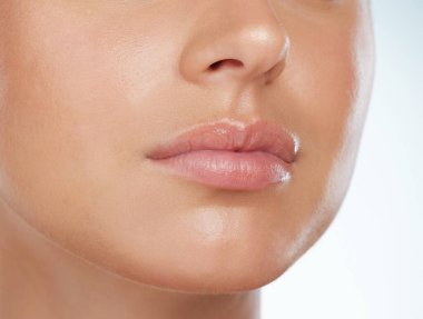 Closeup of perfect lips on unknown woman in studio. Caucasian model with smooth glowing skin isolated against a grey background and posing. Woman with healthy luscious plump lips and routine lip care.