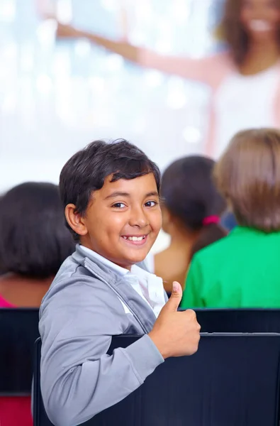 渴望年轻的心灵 一个小男孩坐在教室里给你竖起大拇指的画像 — 图库照片