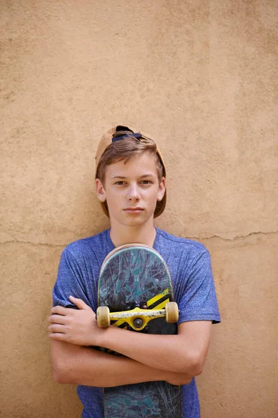 スケートボードは彼の心に近い 壁に立っている間に彼のスケートボードを保持している10代の少年の肖像 — ストック写真