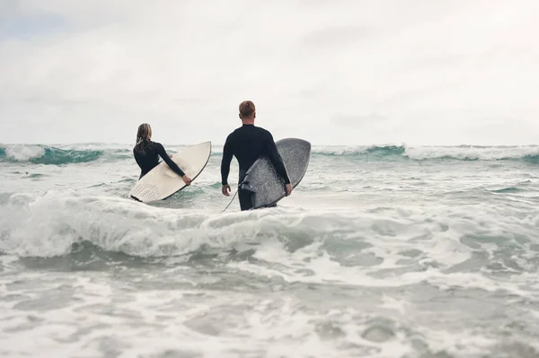 波がある所にサーファーがいる 若いカップルがサーフボードを持って海に出て — ストック写真