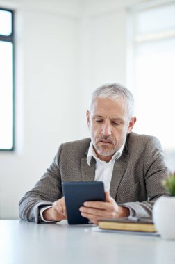 Her şey bir düğmeye basarak. Yetişkin bir işadamı, ofiste bir masada otururken dijital tablet kullanıyor.