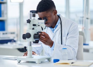 Bu deney gerçekleşiyor. Odaklanmış genç bir bilim adamı test örneklerine gün içinde bir laboratuvarın içinde mikroskopla bakıyor.
