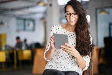 Son iş eğilimlerinin başında kalıyor. Modern bir ofiste otururken dijital tablet kullanan genç bir kadın.