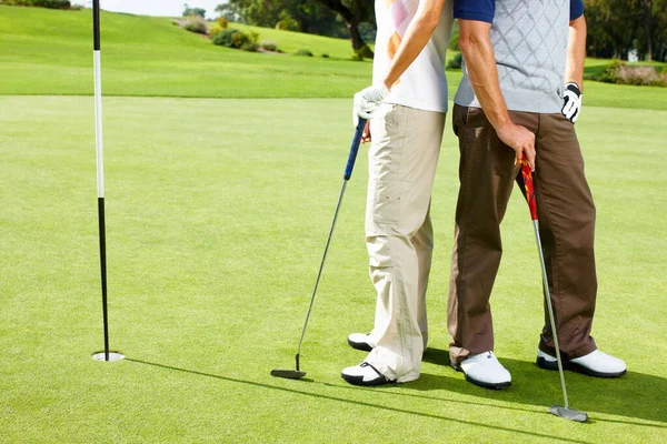 フラグスティックの近くに立ってゴルフカップル 低セクションのカップル立っている上に置く緑の近く鞭と保持ゴルフクラブ — ストック写真