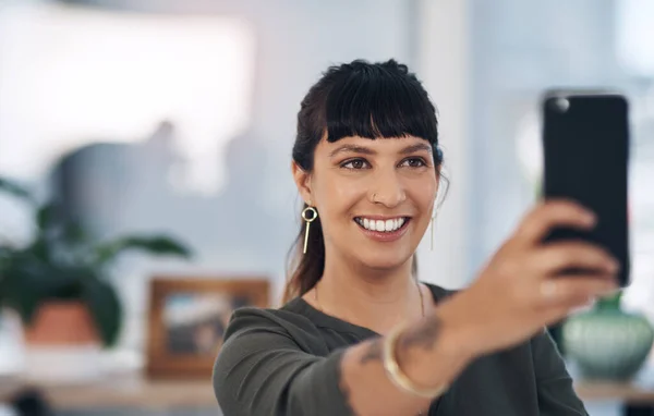 stock image A selfie a day keep self-doubt away. an attractive young businesswoman sitting alone in her office and using her cellphone to take a selfie