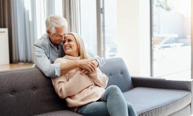 Aşk mutlu bir yuva yapar. Olgun bir adam evdeki kanepede karısına sarılıyor.