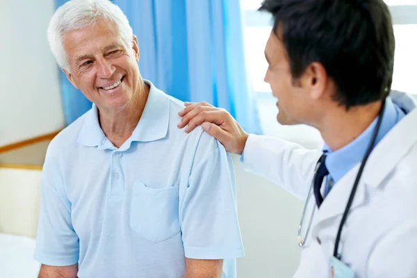 stock image Doctor, senior man patient and discussion with smile, medical clearance and news for healthy in clinic. Men, happy medic and consultation for wellness, healthcare and talking in hospital for helping.