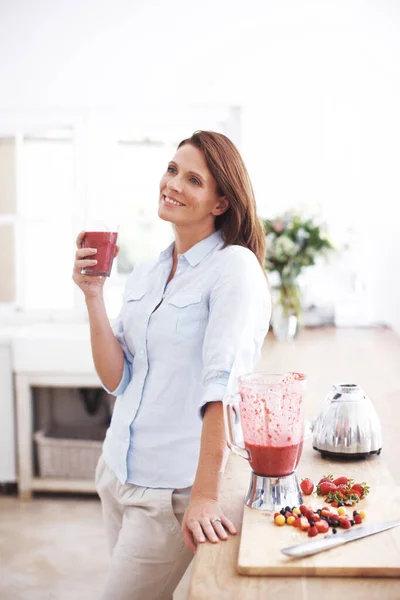 光滑的喜悦 一个漂亮的女人靠着厨房的柜台 享受着水果的柔滑 — 图库照片