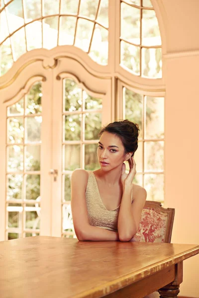 High society beauty. Portrait of a beautiful young woman sitting at a table in her elegant home