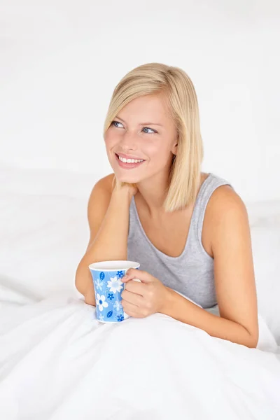 暖かいコーヒーカップで目を覚ます ベッドに座っている間に魅力的な若い女性がコーヒーを飲む — ストック写真