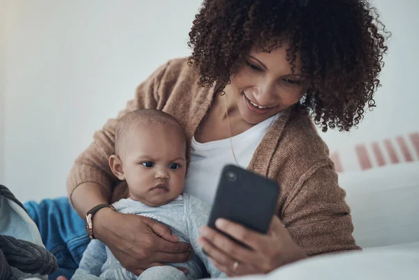 一个很棒的新应用为一个新妈妈 一个年轻的女人在家里和她可爱的女儿在床上休息的时候用智能手机 — 图库照片