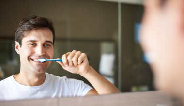 Brushing teeth, man and cleaning in a bathroom at home for oral hygiene and health. Smile, dental and toothbrush with a male person with happiness in the morning at a house with mirror reflection. clipart