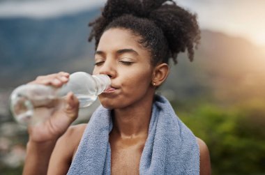 Artık sakinleşebilirsin. Spor yapan genç bir kadın dışarıda egzersiz yaparken su içiyor.