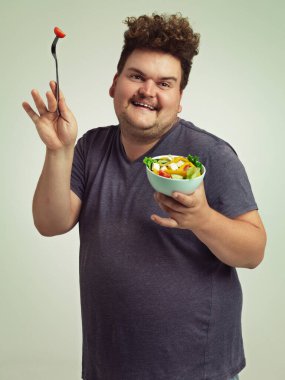 The salad dance. Studio shot of an overweight man holding a bowl of salad in a silly pose