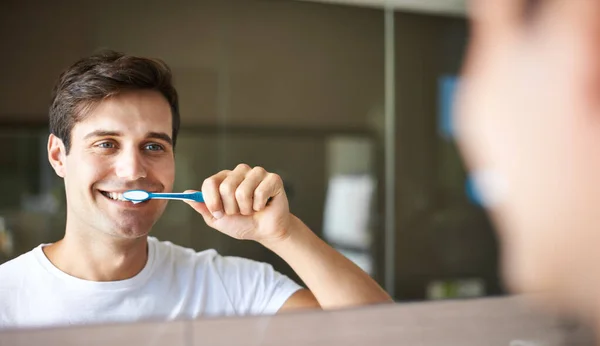 Brushing teeth, man and cleaning in a bathroom at home for oral hygiene and health. Smile, dental and toothbrush with a male person with happiness in the morning at a house with mirror reflection.