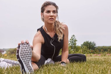 Yakıtın olarak odaklan. Spor yapan genç bir kadın dışarıda egzersiz yaparken bacaklarını açıyor.