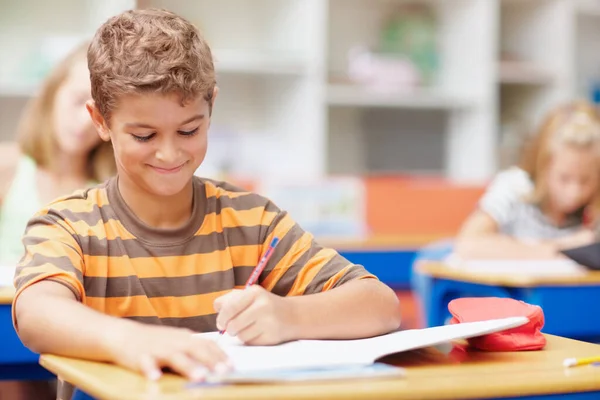 他从他的教育中得到了最大的好处 可爱的男孩在课间休息时坐在课桌前微笑着记笔记 — 图库照片