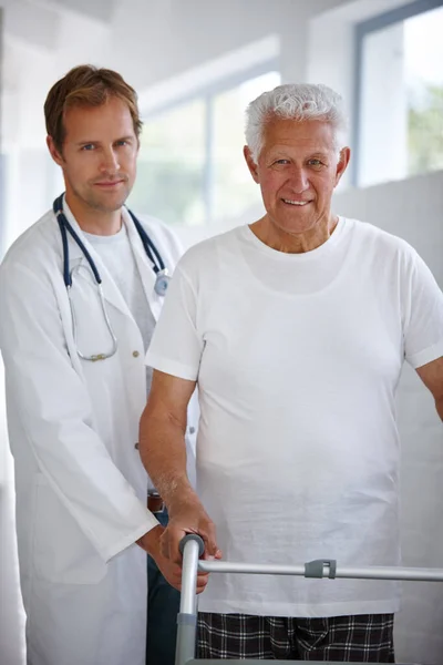 stock image Its OK to need assistance. Portrait of a male doctor standing with his senior patient whos using a walker for support