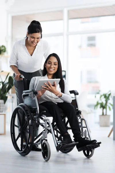 Tell me what you think...Full length shot of an attractive young businesswoman in a wheelchair talking to the female colleague pushing her through the office