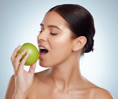 Fotokopi çekerken yeşil elmayı ısıran güzel bir kadın. Beyaz model bir stüdyoda gri bir arka planda izole edilmiş. Sağlıklı beslenmek ve sağlıklı beslenmek iyi bir cilt bakımının parçasıdır..