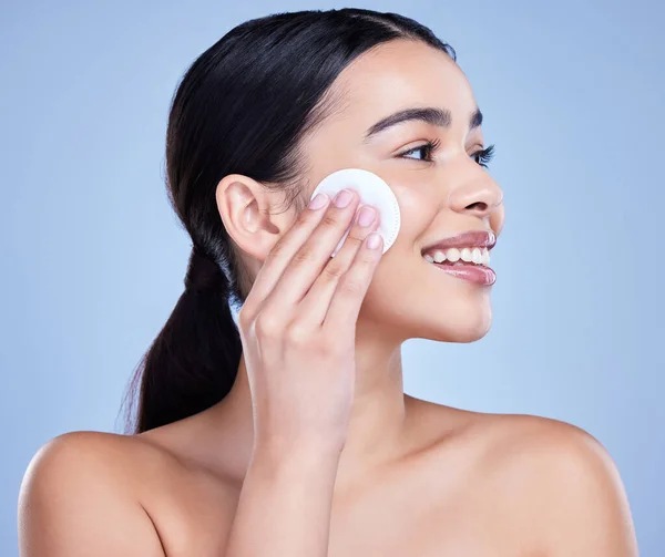 stock image A beautiful smiling mixed race woman using a cotton pad to remove makeup during a selfcare grooming routine. Hispanic woman applying cleanser to her face against blue copyspace background.