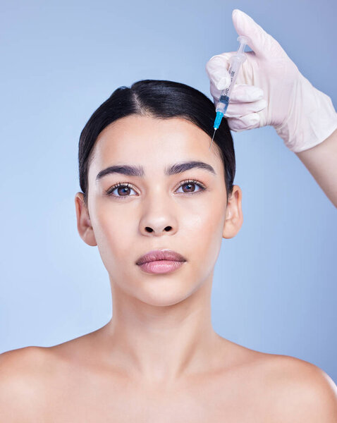 Studio portrait of a gorgeous mixed race woman getting botox filler. Hispanic model getting cosmetic surgery against a blue copyspace background.