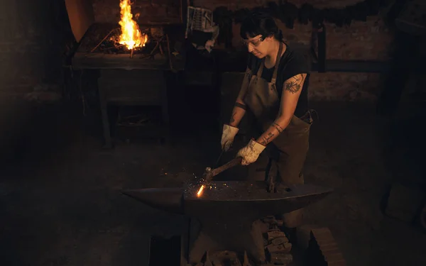没有什么比用手工作更有回报的了在铸造厂用铁锤击打热金属棒的年轻女子 — 图库照片
