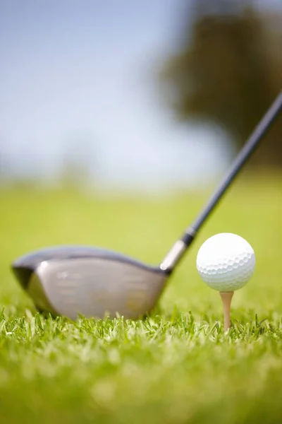 Club and golf ball. Golf ball carefully balanced on a golf tee with a club in the background