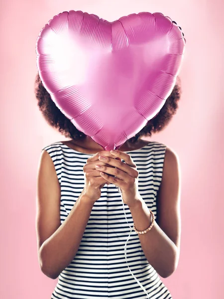 Woman cover face with heart balloon in studio, pink background and celebrate surprise birthday party. Female model hide with helium, gift and present for love, valentines day and secret celebration.