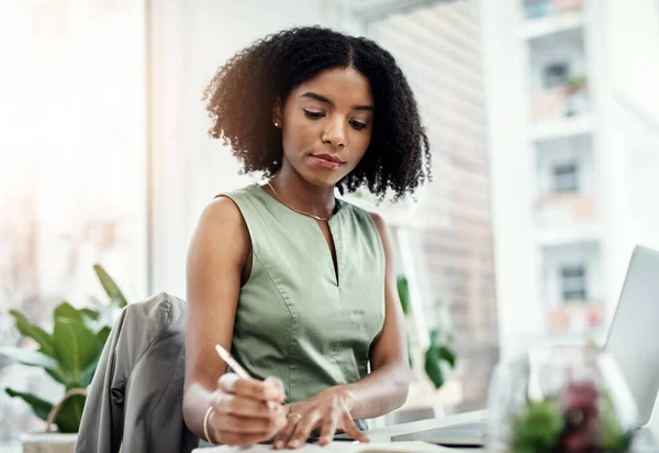 オフィスの机に座っている本やノートパソコンで書いている企業 黒人のビジネス女性 職場でのアフリカの女性労働者の計画スケジュール リマインダと焦点を当てた情報に関するメモを書く — ストック写真