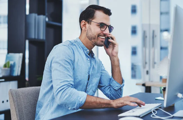 stock image Let me open those files online...a young designer talking on a cellphone while working on a computer in an office